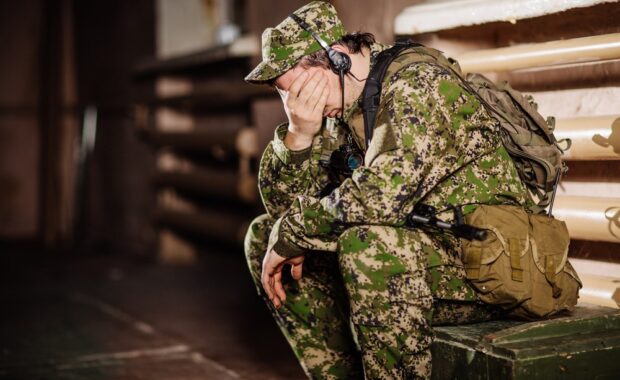 man dressed in military uniform sitting on a green box and covering his eyes