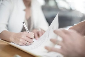 woman signing contract at desk at car dealership